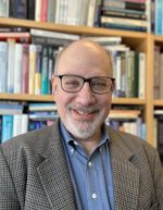 Dr. Levy from the chest up, wearing a brown suit and blue shirt smiling